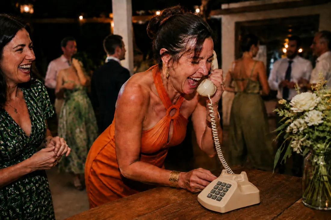Friends leave a joyful message on an audio guestbook phone at a wedding reception.